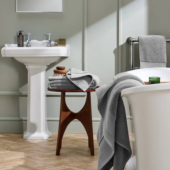 Bathroom with a sink, stool, and bathtub draped with gray towels.