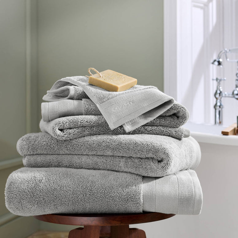 Stack of gray towels on a wooden stand with a bar of soap in a bathroom setting.