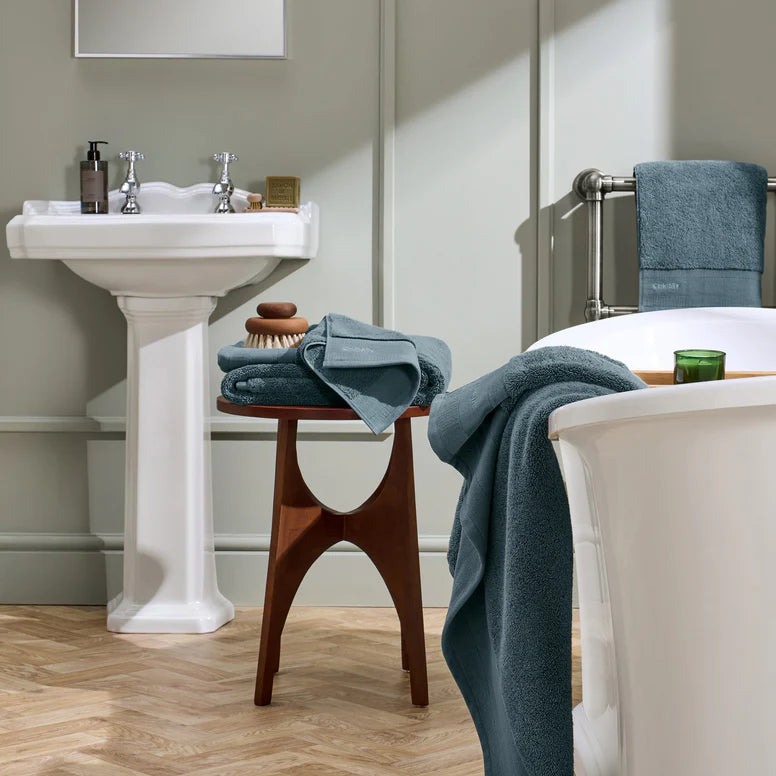 Bathroom with white sink, wooden stool, and bathtub with blue towels.