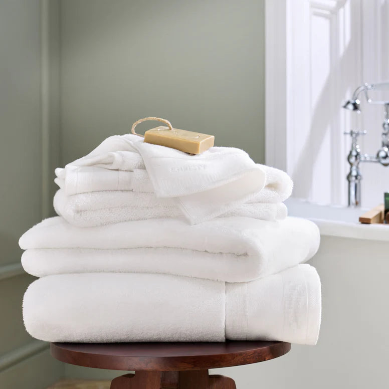 Stack of white towels on a wooden stool with a bar of soap in a bathroom setting