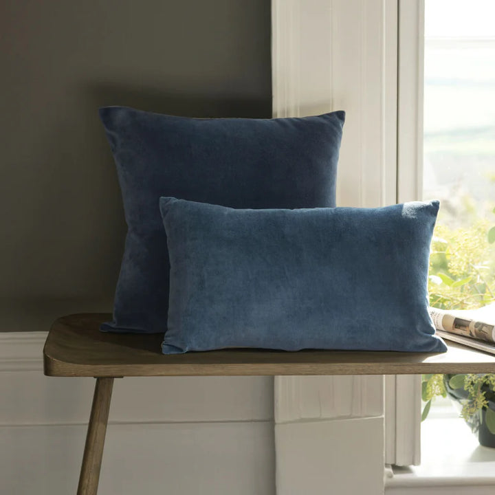 Two blue pillows on a wooden stool by a window with natural light.