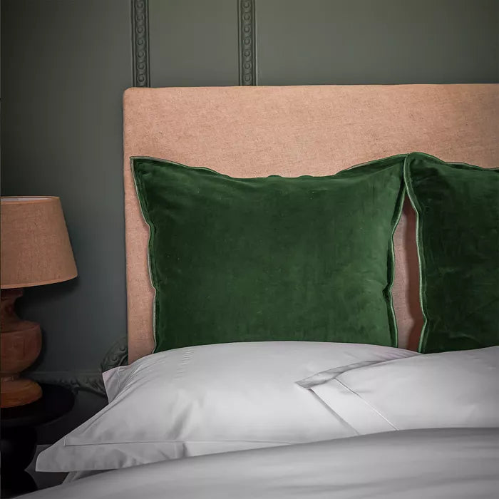 Green pillow on a bed with a beige headboard against a dark green wall.