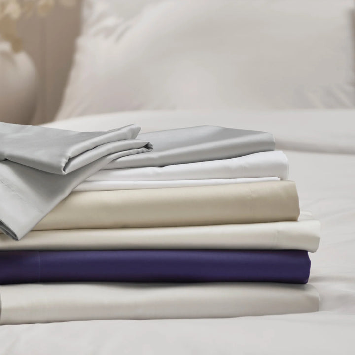 Stack of folded bed sheets in various colors on a bed.