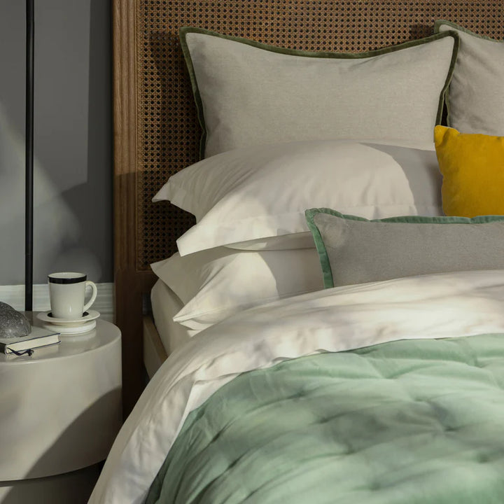 Bed with green and white bedding, yellow pillow, and a nightstand with a cup.