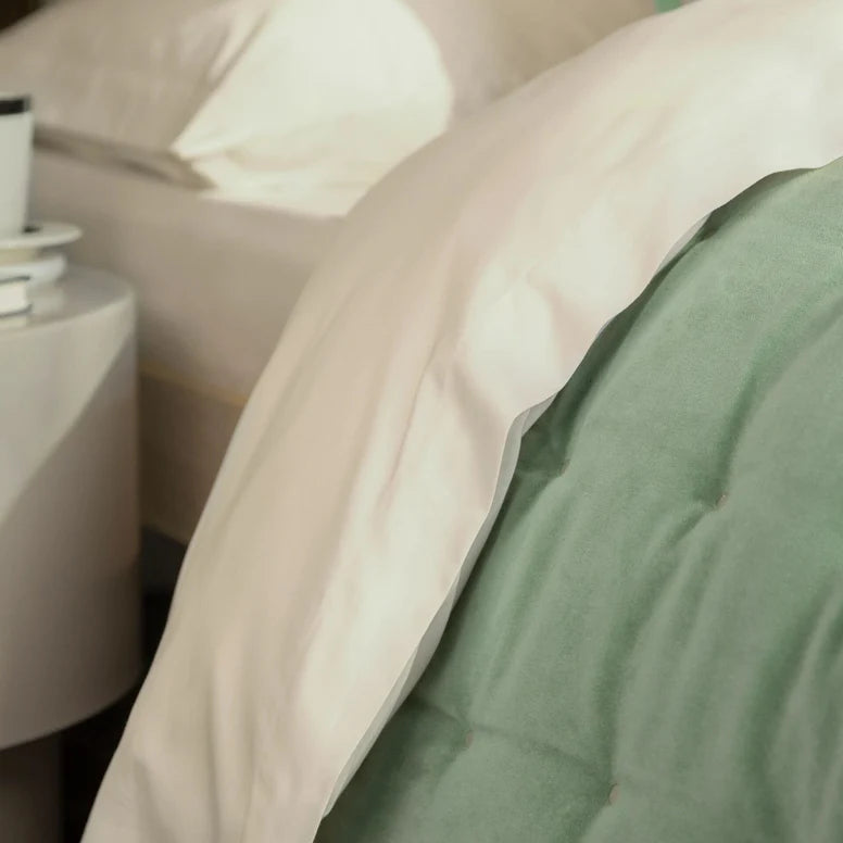 Close-up of a green blanket on a bed with a side table in the background