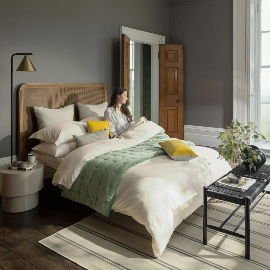 Woman sitting on a bed in a bedroom with a green blanket and yellow pillows.