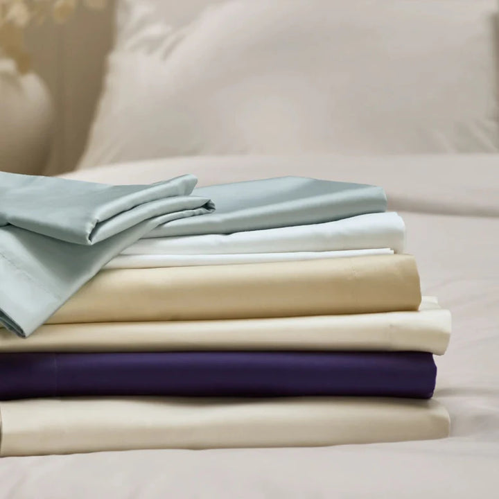 Stack of folded bed sheets in various colors on a bed.