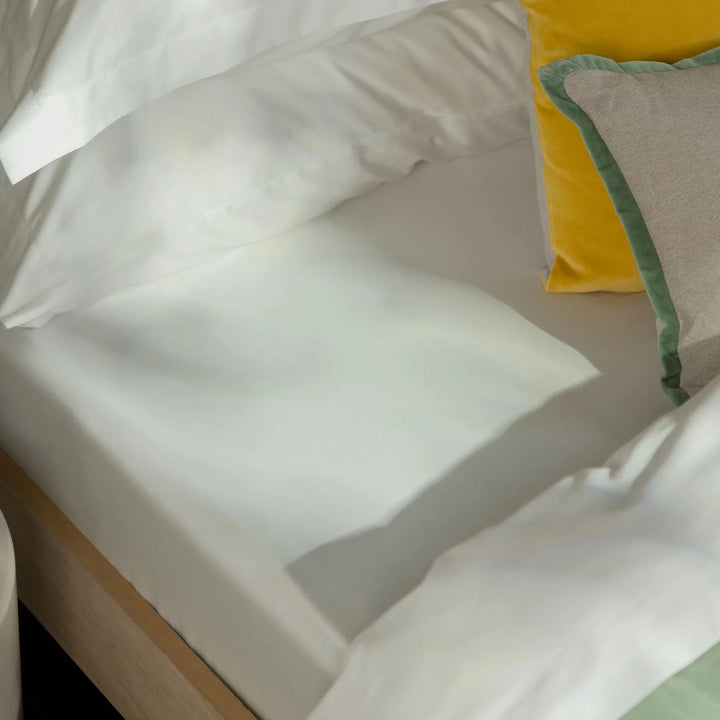 Close-up of white pillows on a bed with a yellow and green pillow in the corner.