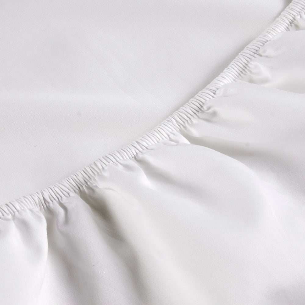 Close-up of a white fitted sheet on a bed with a plain background