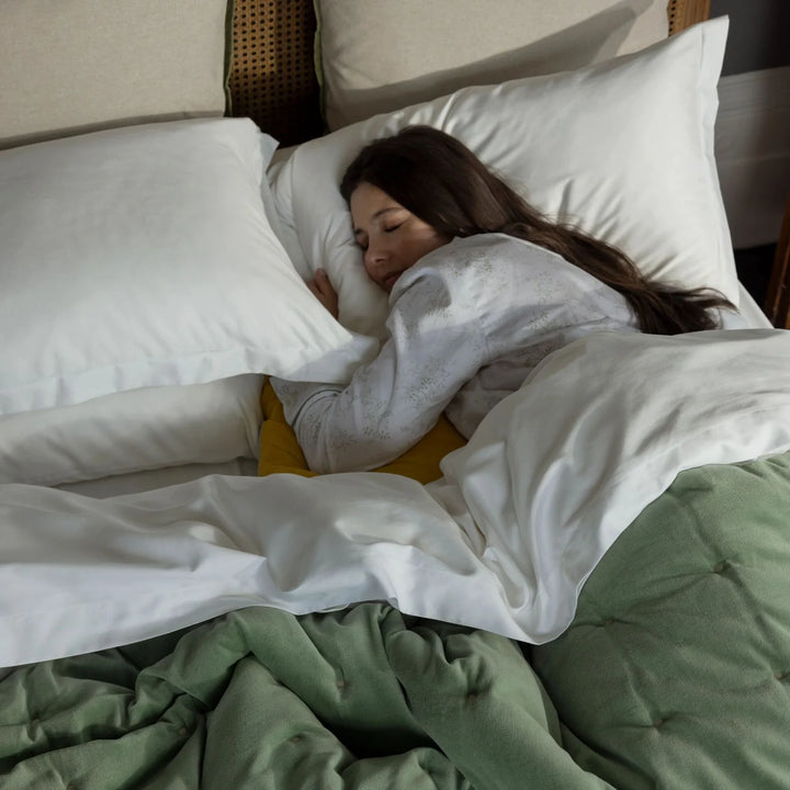 Woman sleeping in a bed with white pillows and green blanket