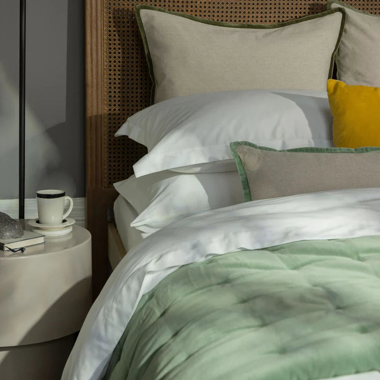 Bed with green and white bedding, yellow pillow, and side table with cup.