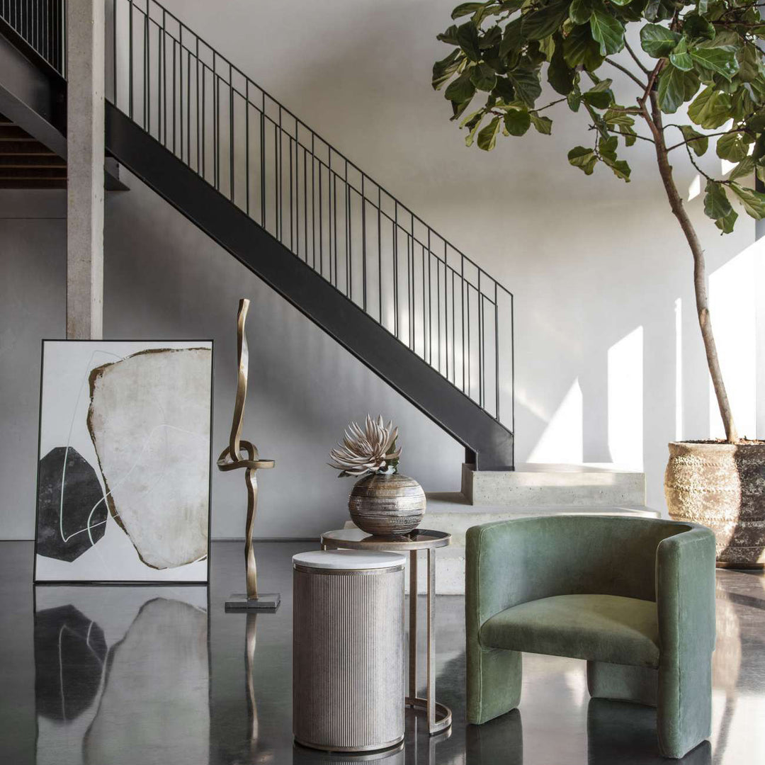 Modern interior with a green armchair, decorative plant, and abstract art on a wall.