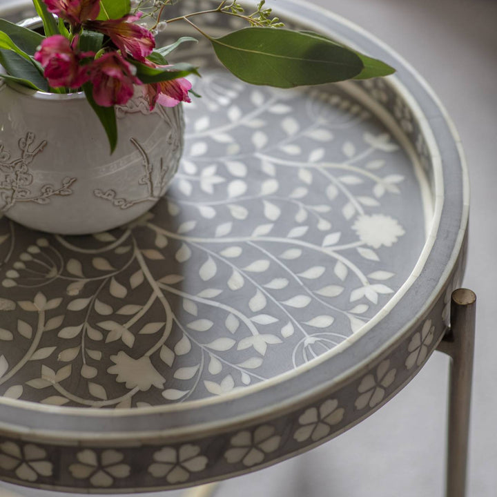 Round decorative table with floral pattern and a vase of flowers on a neutral background