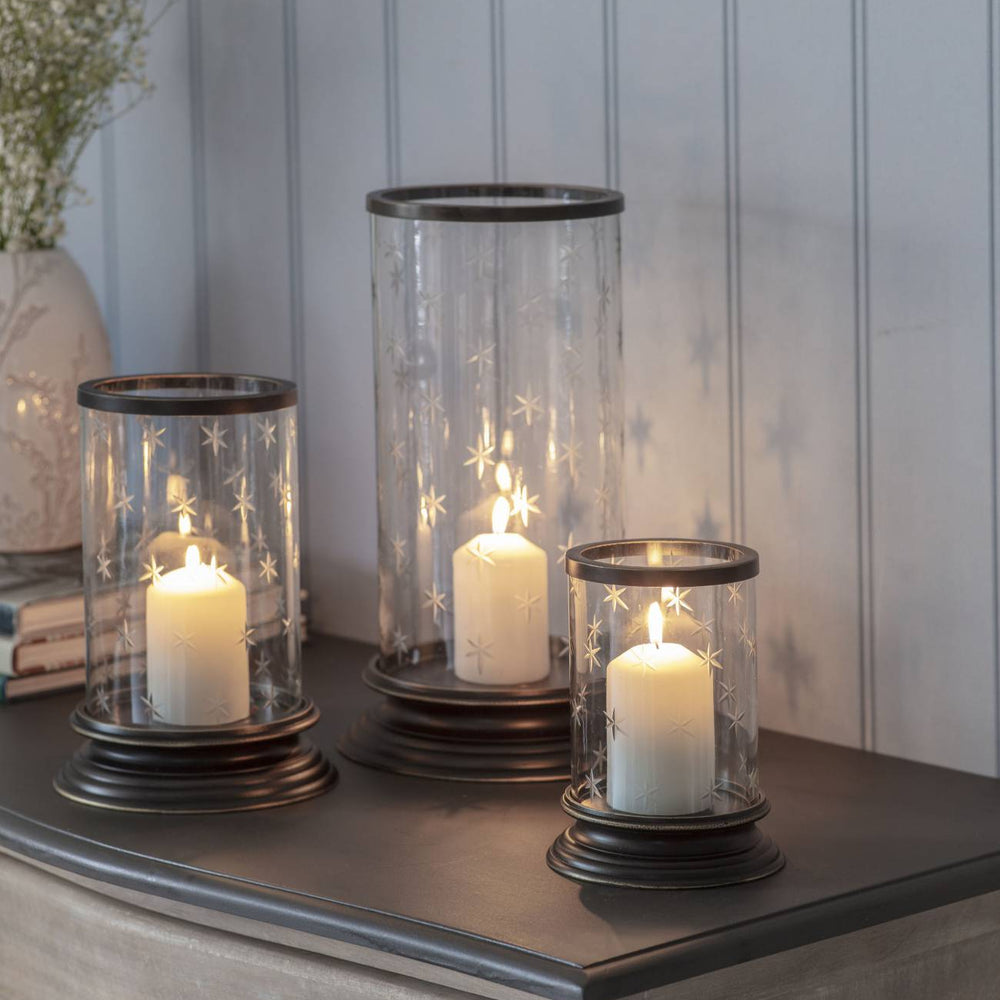 Three candle holders with candles on a wooden surface against a light gray wall.