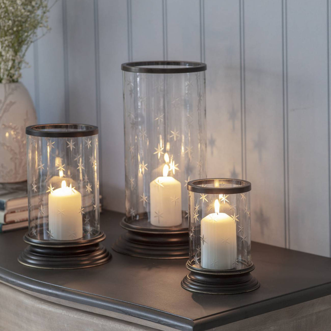 Three candle holders with candles on a wooden surface against a light gray wall.