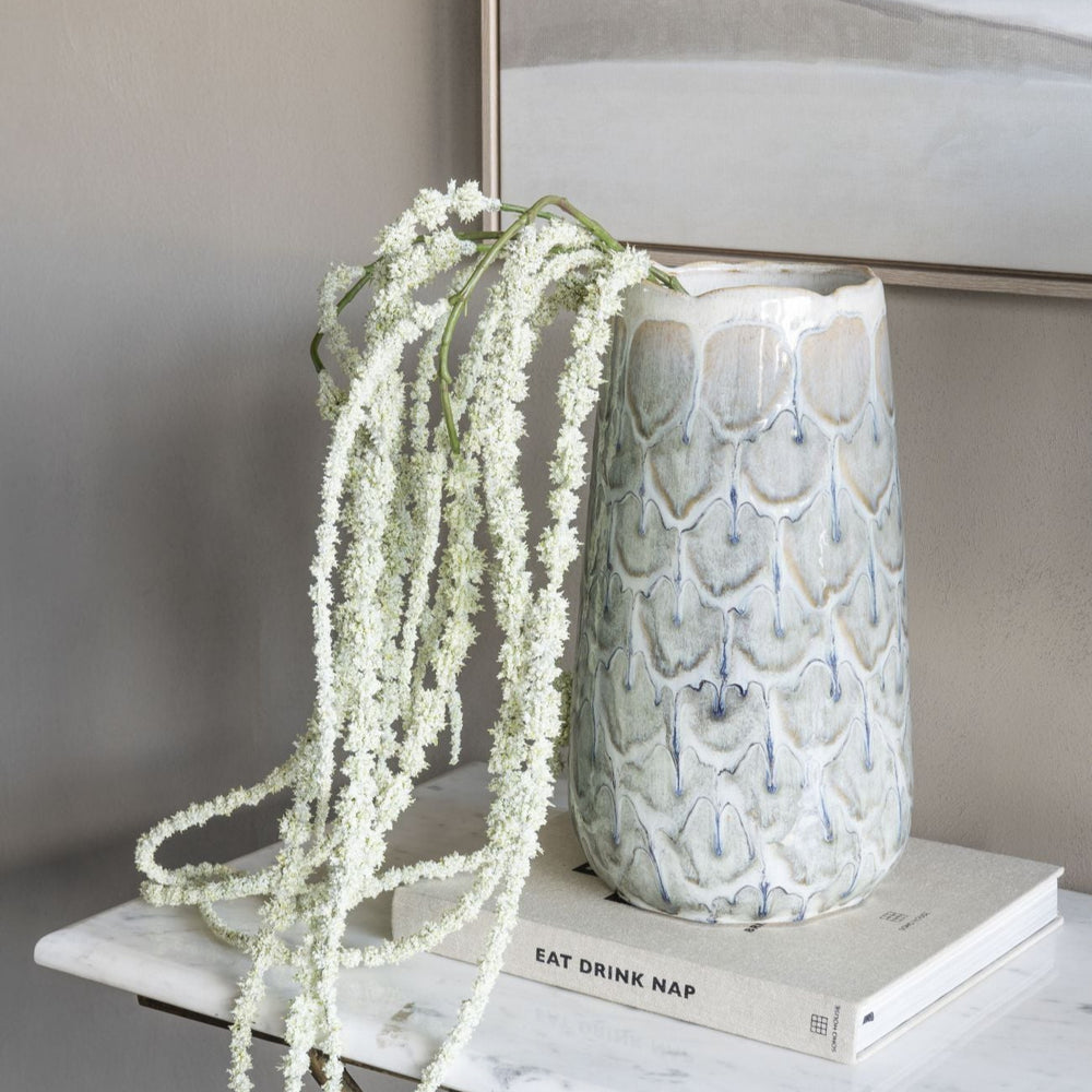 Decorative vase with textured surface on a marble surface next to a plant