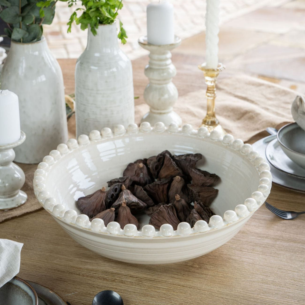 White decorative bowl with dark objects on a table setting with candles and flowers.