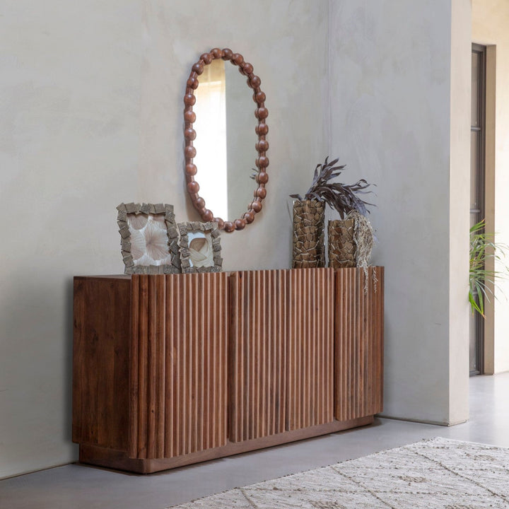 Wooden sideboard with decorative items against a plain wall.