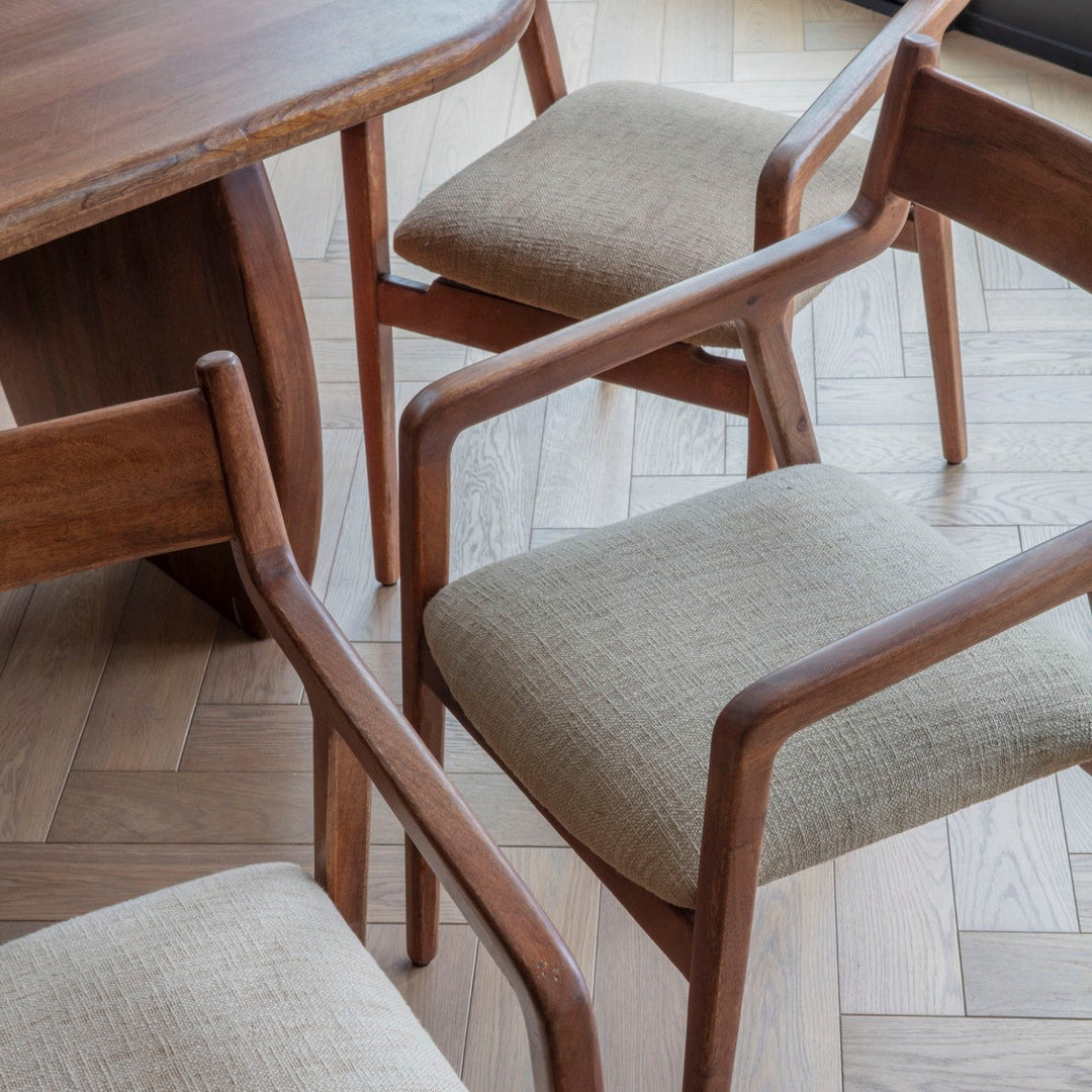 Wooden chairs with beige cushions around a wooden table on a herringbone floor.