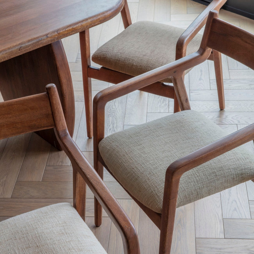 Wooden chairs with sage cushions around a wooden table on a herringbone floor.