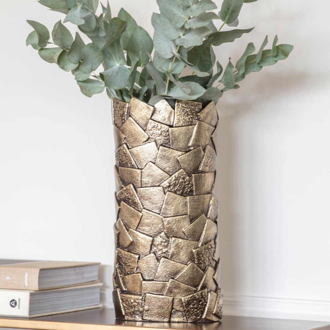 Bronze textured vase with greenery on a white surface