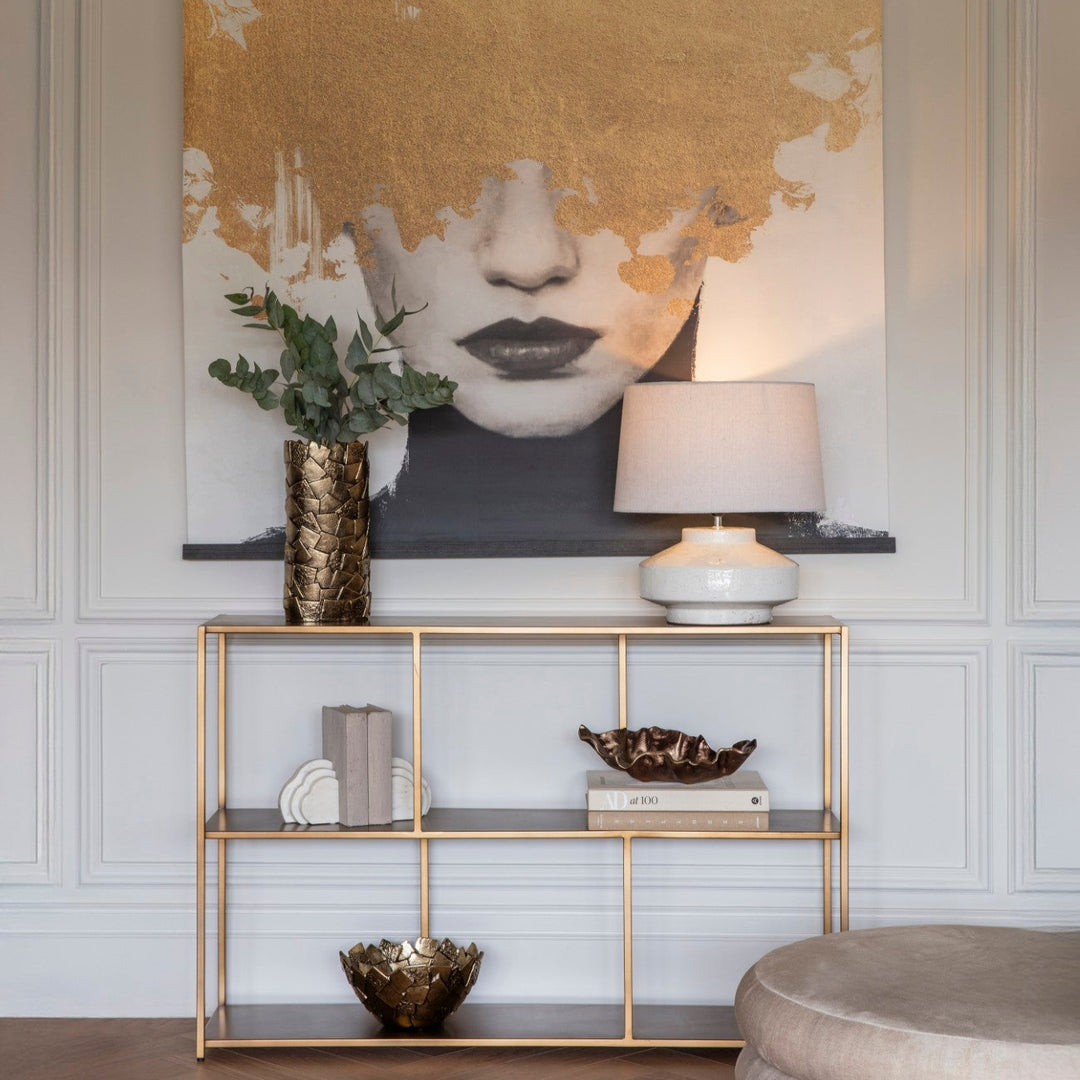 Decorative wall art with abstract design in a room with a gold shelf and lamp.