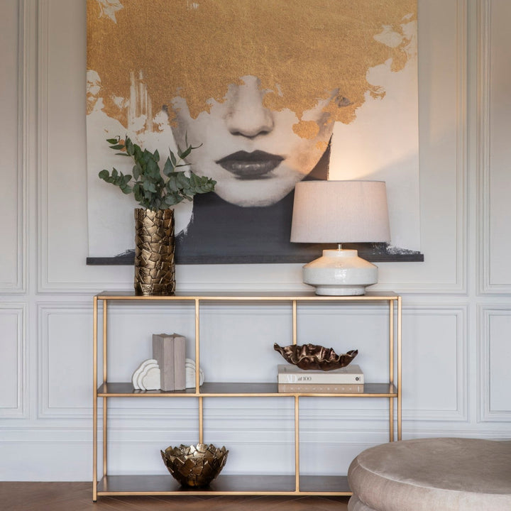 Decorative wall art with abstract design in a room with a gold shelf and lamp.