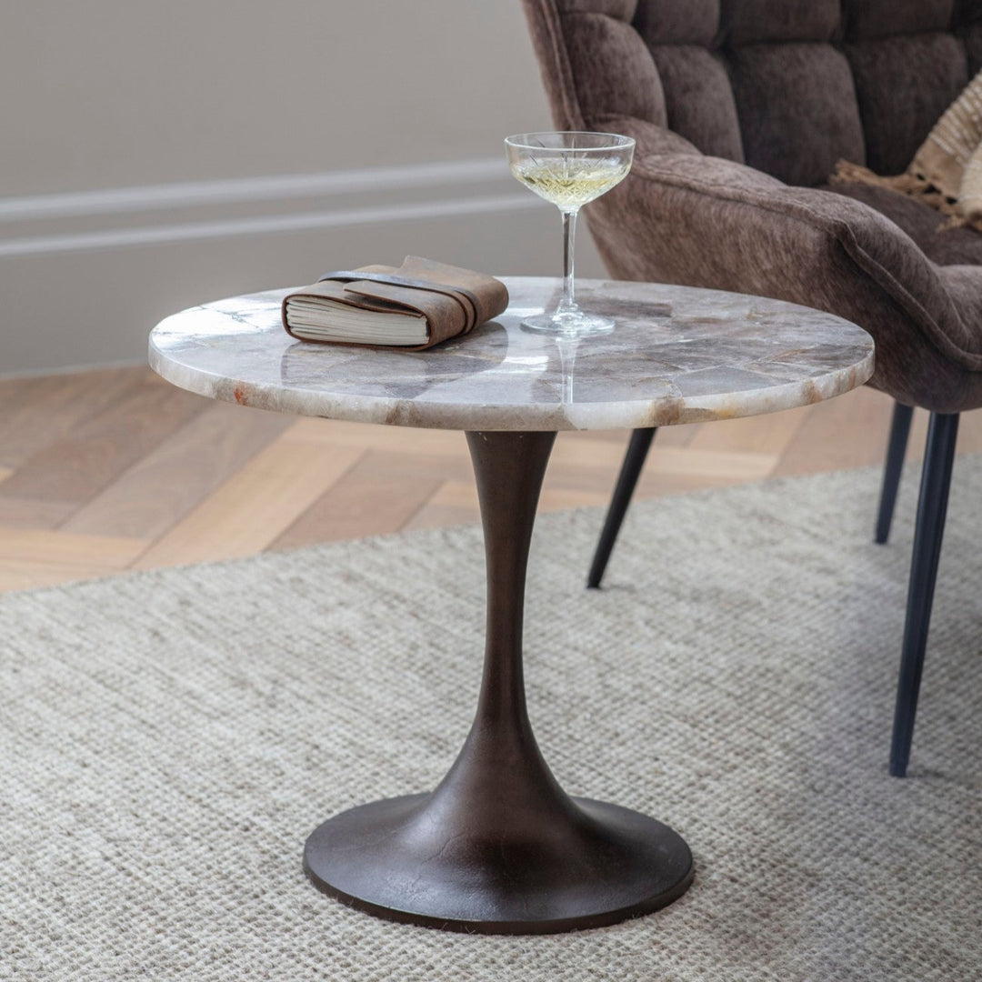 Round marble coffee table with a glass of white wine and a book in a living room setting.