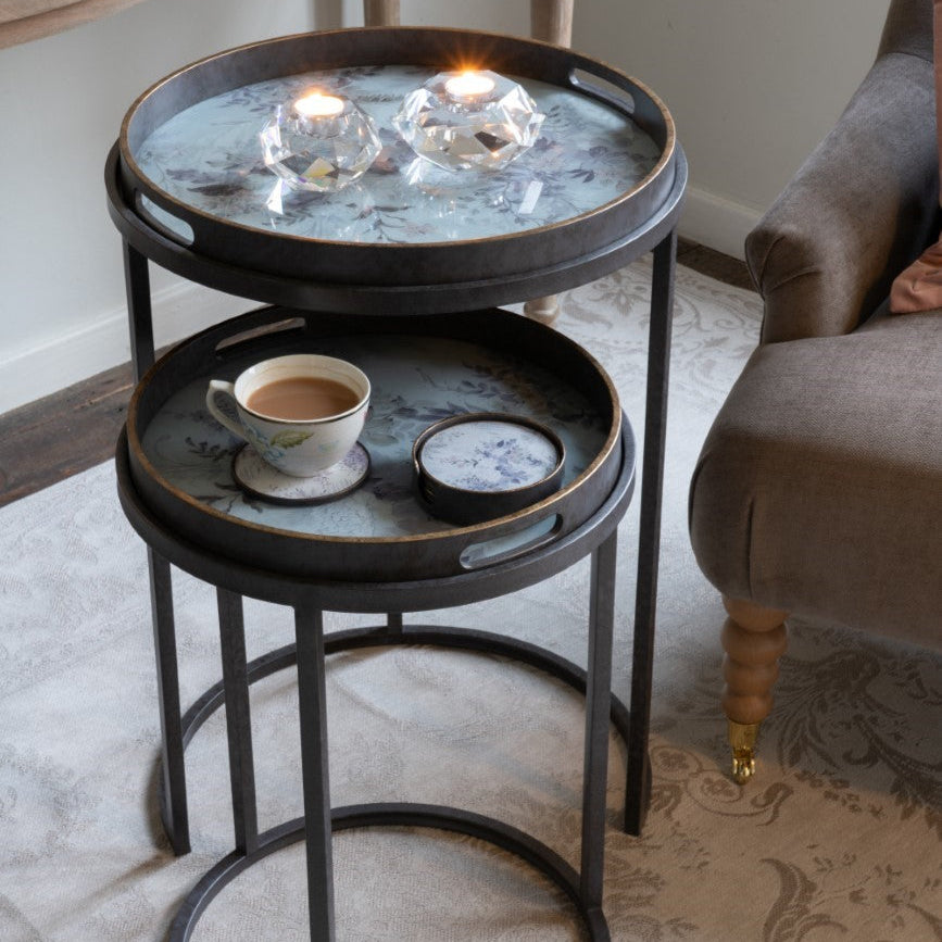 Small round metal table with a cup of coffee and decorative items on a carpeted floor.
