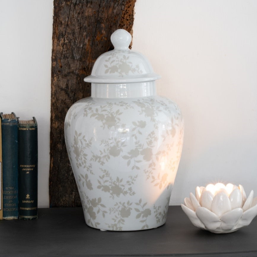 White textured ceramic jar with a lid on a wooden surface with a white wall and books in the background.