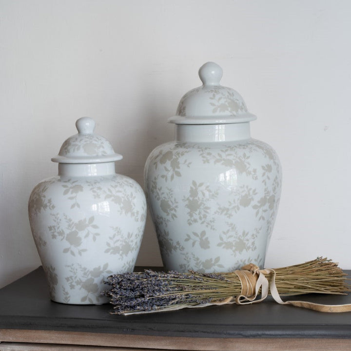 Two white ceramic jars with floral patterns on a wooden surface with a broom and lavender.