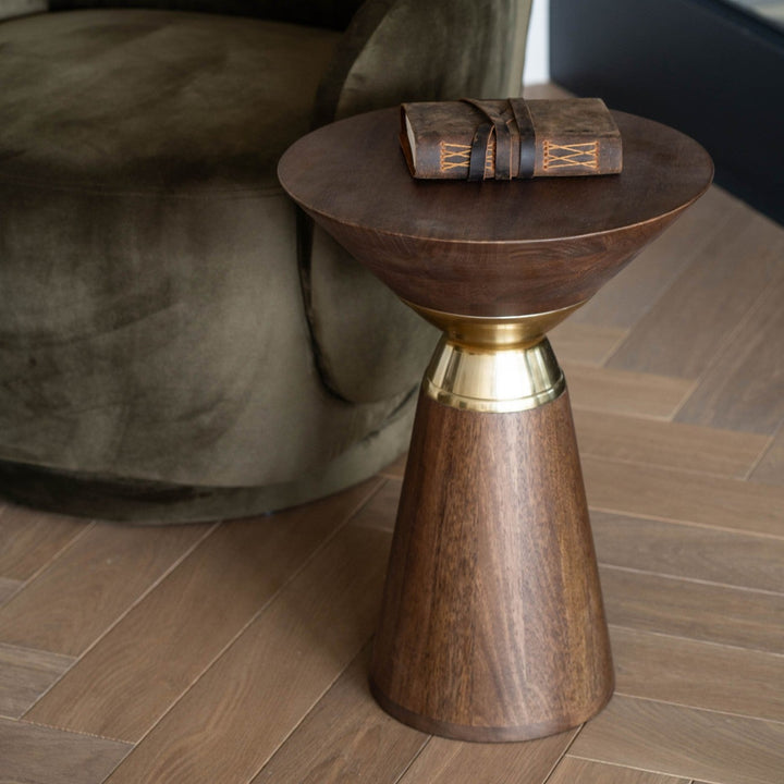 Wooden side table with gold accent next to a green armchair on a wooden floor.