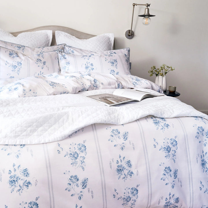 Floral patterned bedding set on a bed with an open book, in a softly lit bedroom.
