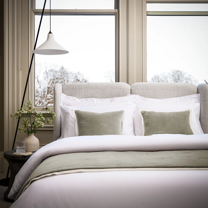 Neatly made bed with white bedding and light green pillows in a bright bedroom.