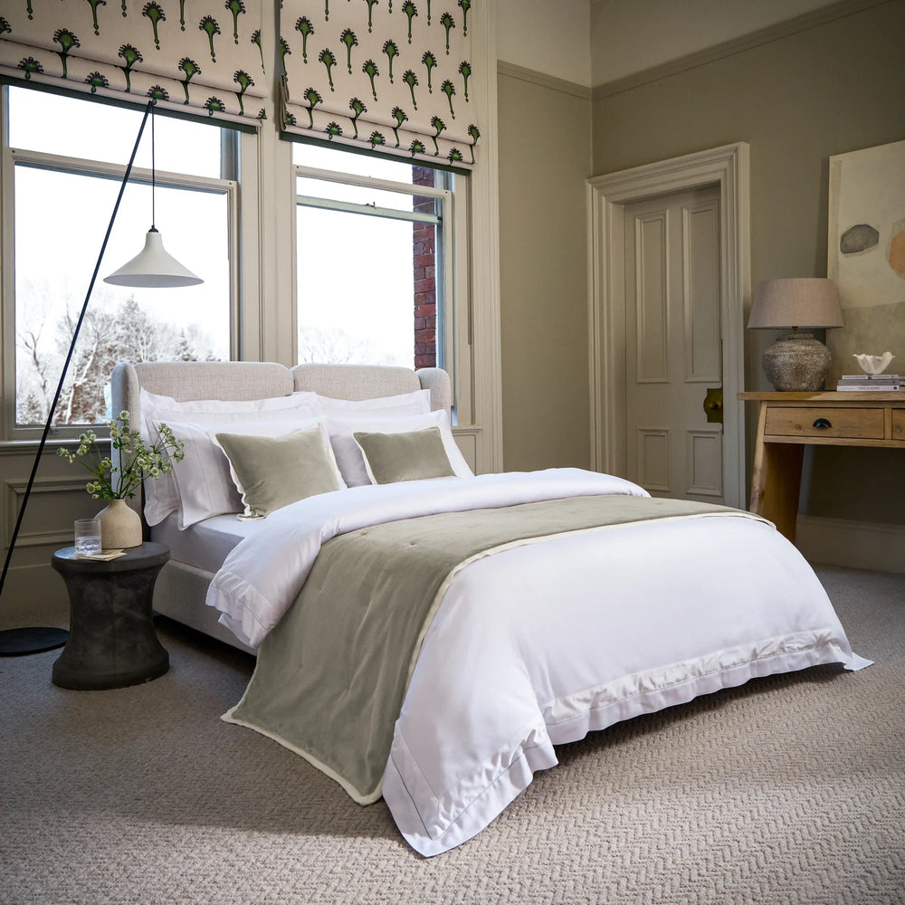 Neatly made bed with white and green bedding in a well-lit bedroom.