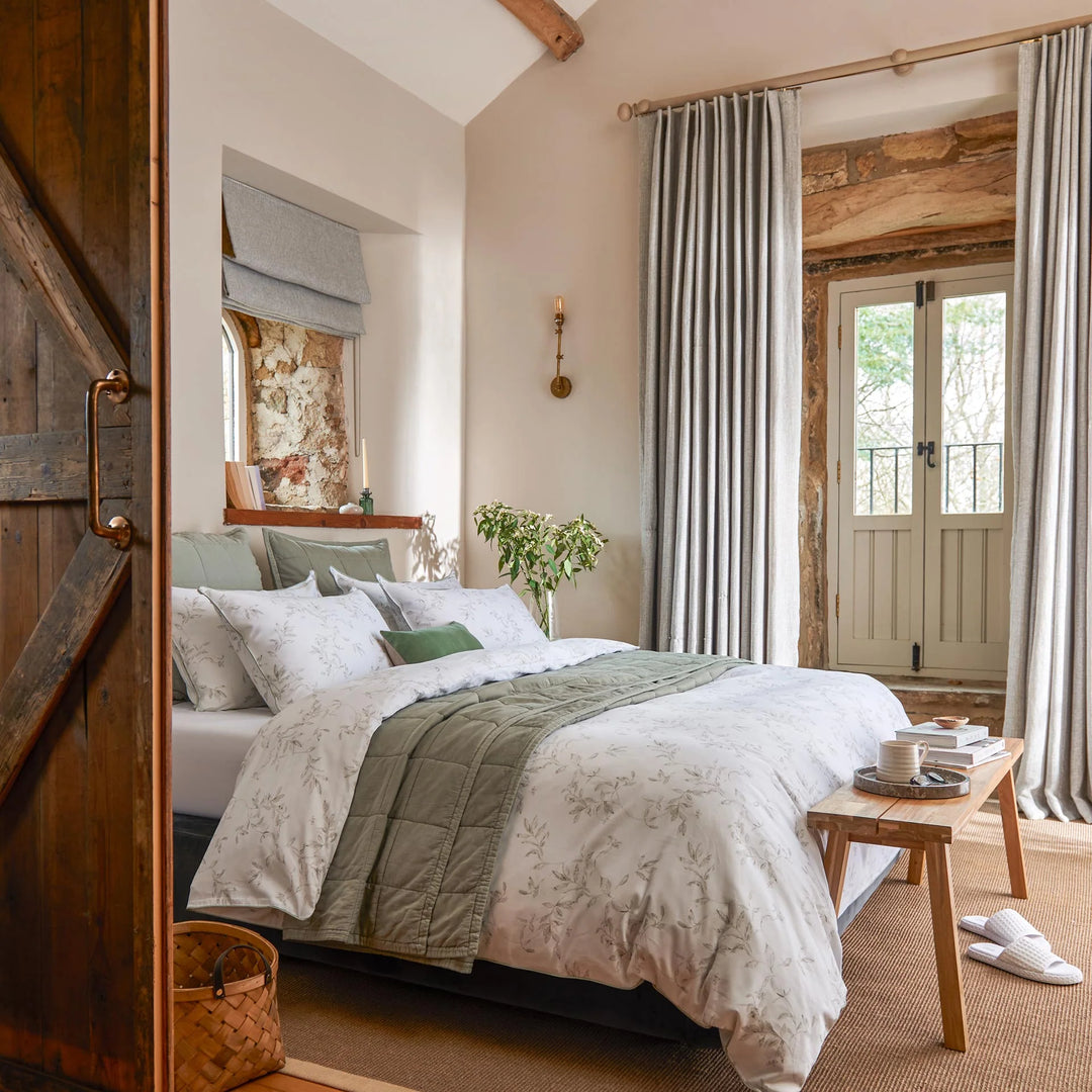Cozy bedroom with wooden door, bed with green and white bedding, and a small table.