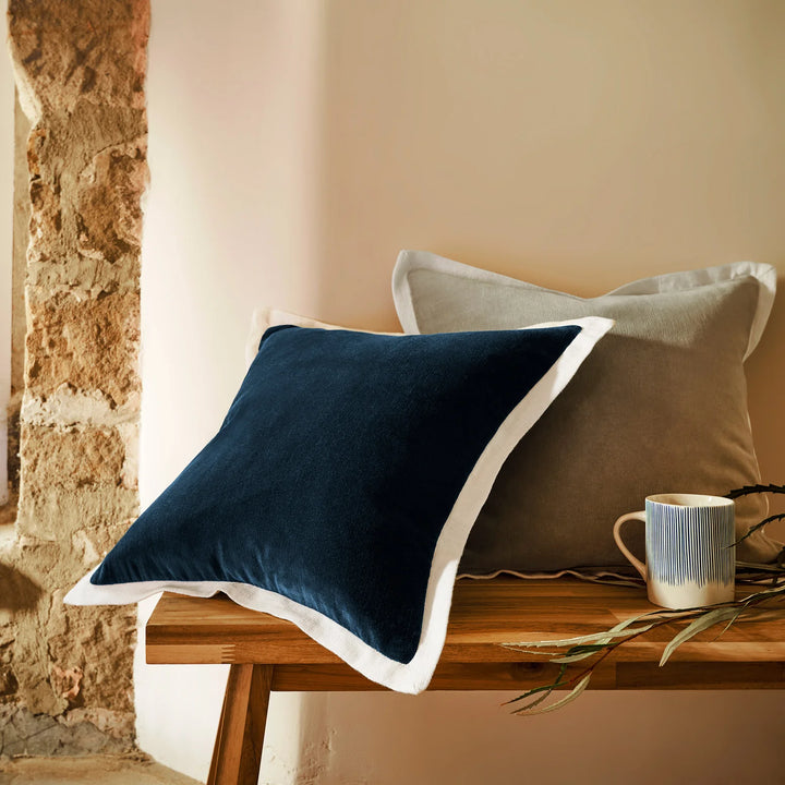 Navy blue pillow and beige cushion on a wooden bench against a stone wall.