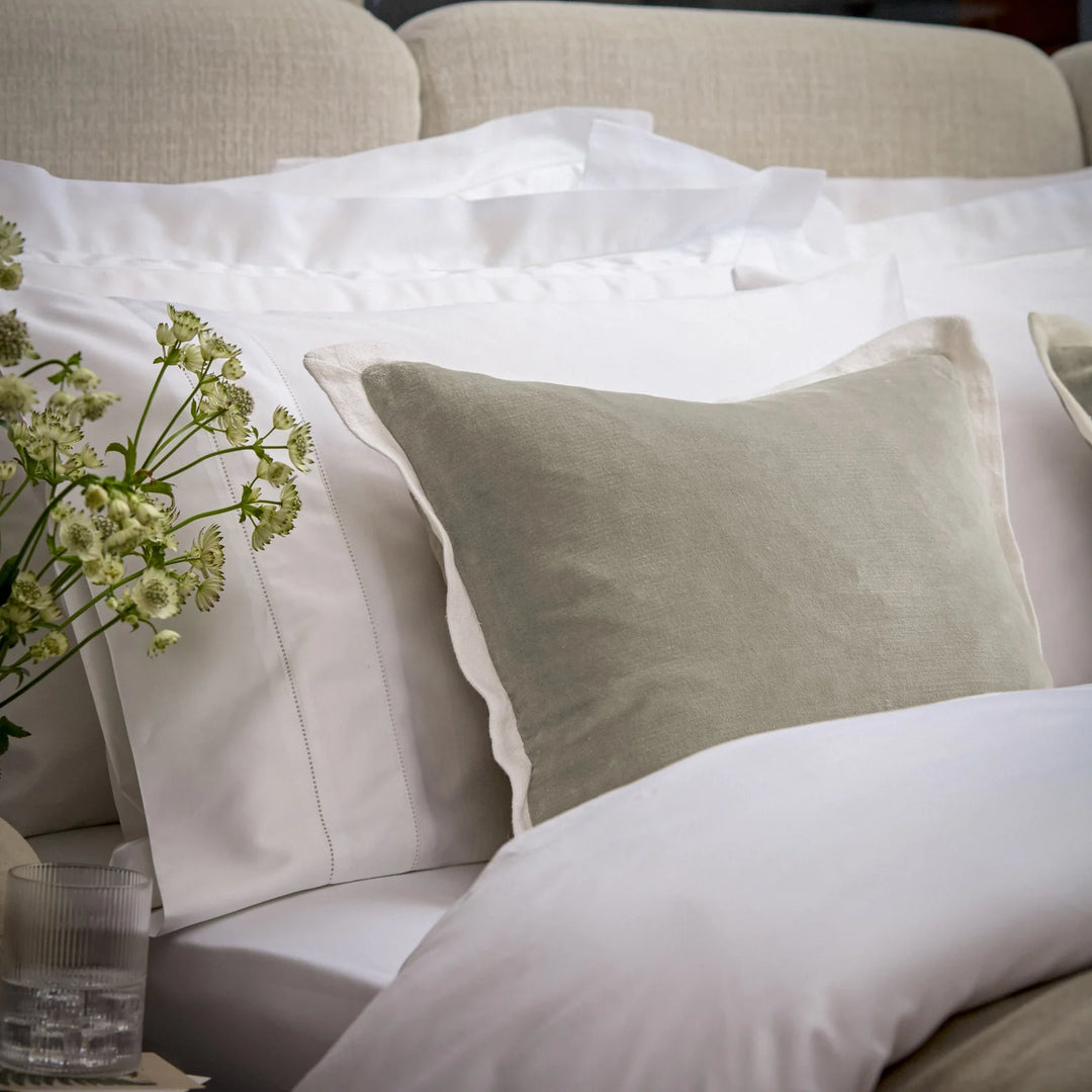 Neatly arranged pillows on a bed with a vase of flowers and a glass.