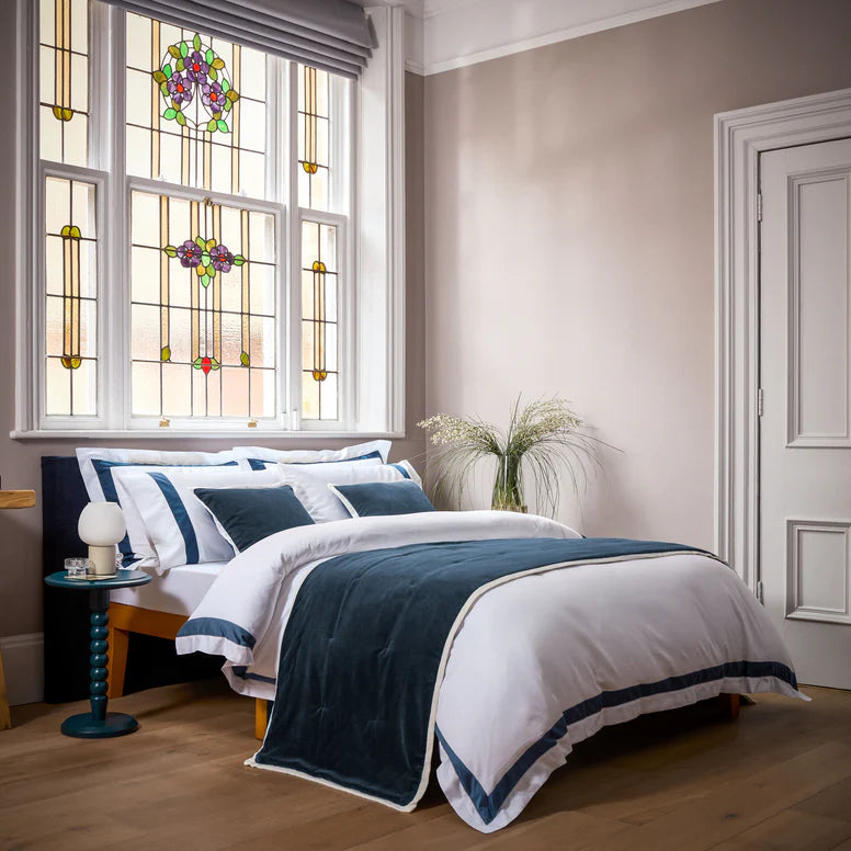 Neatly made bed with blue and white bedding in a bedroom with stained glass window.