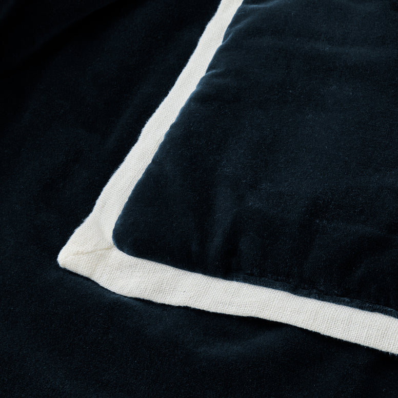 Close-up of a dark blue blanket with white trim on a black background