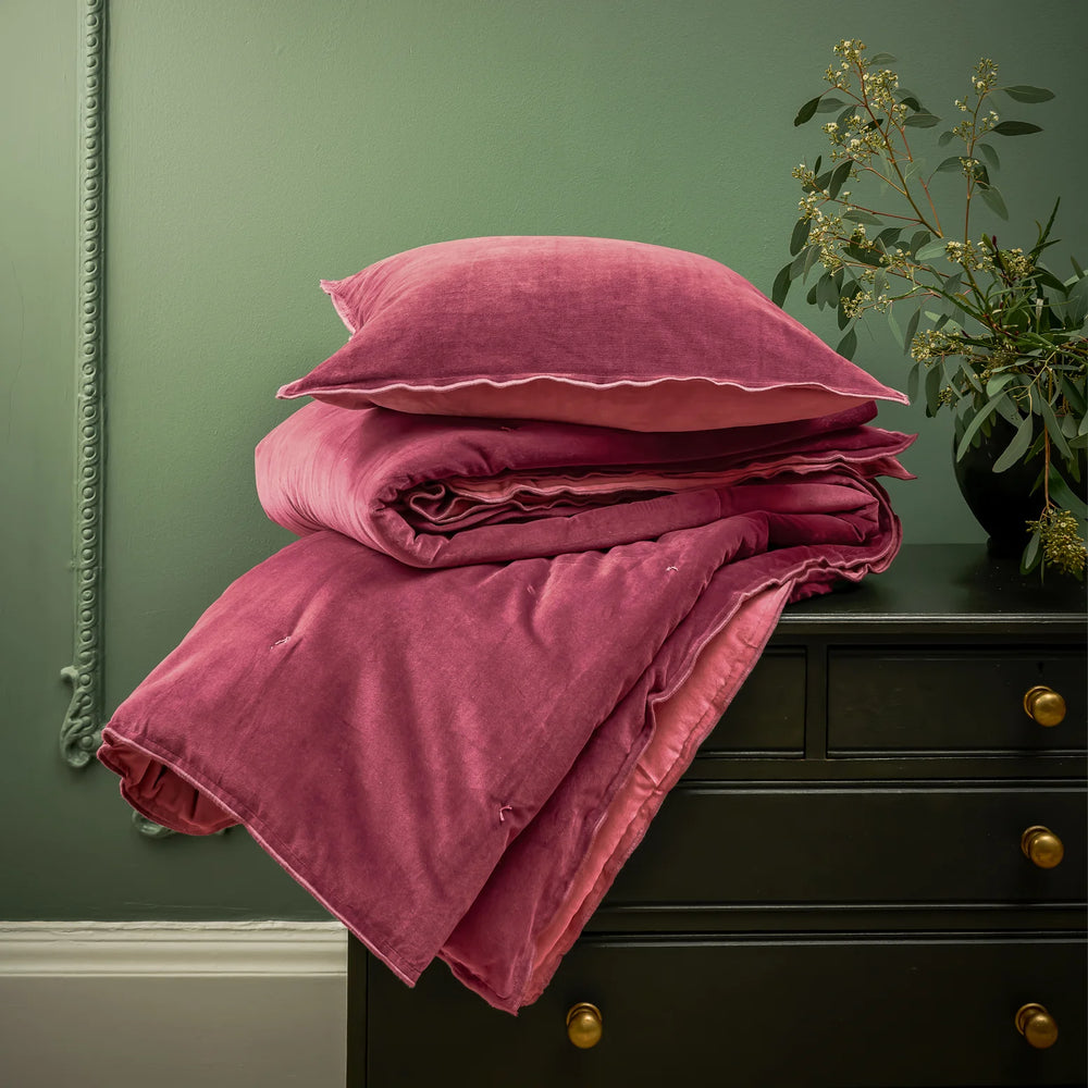 Pink bedding set on a dark green dresser with a plant in the background