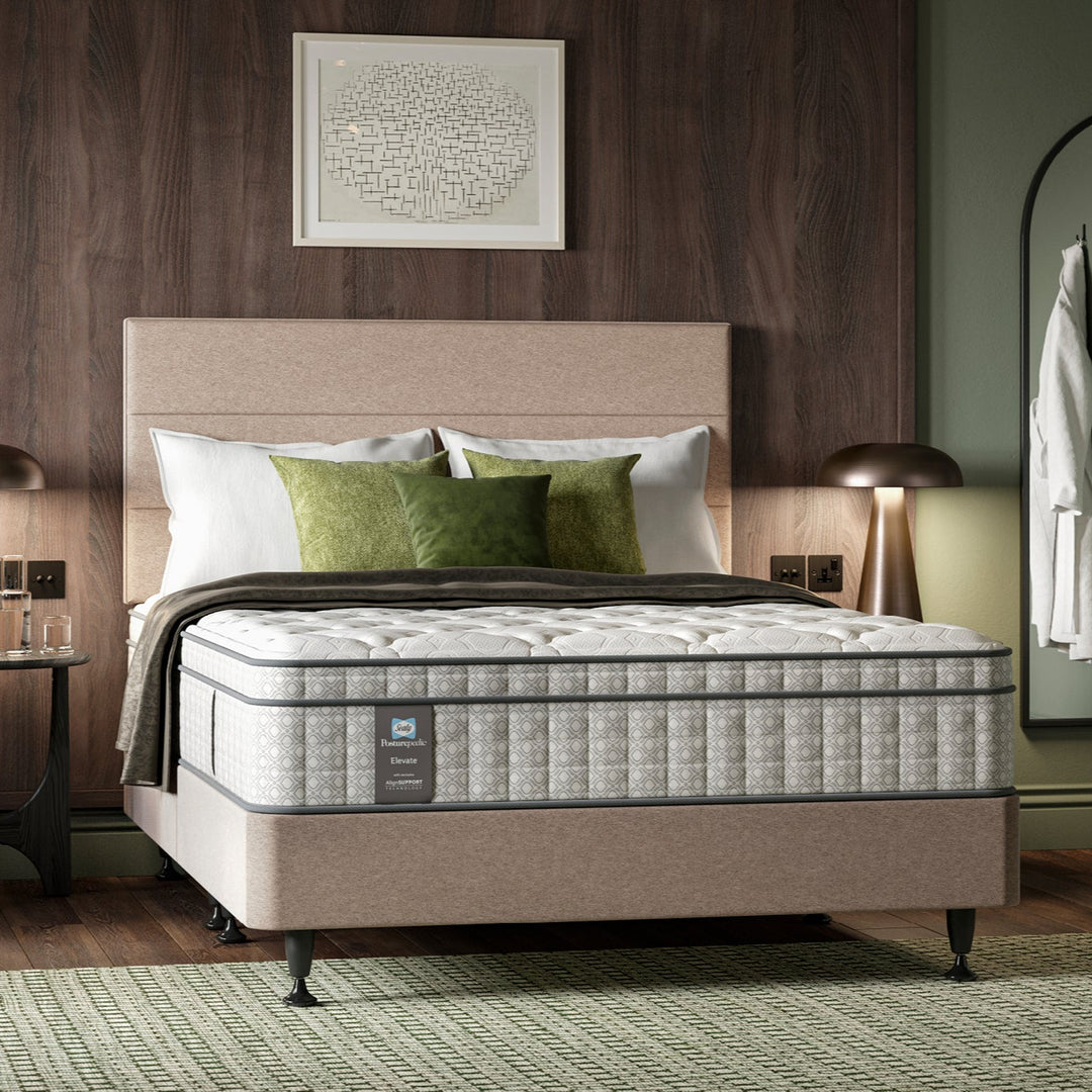 Hotel bedroom with a bed featuring a Sealy Opulence mattress and pillows, wooden headboard, and side tables