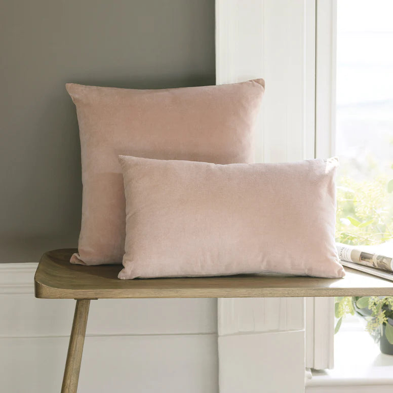 Two pink pillows on a wooden bench by a window with natural light.