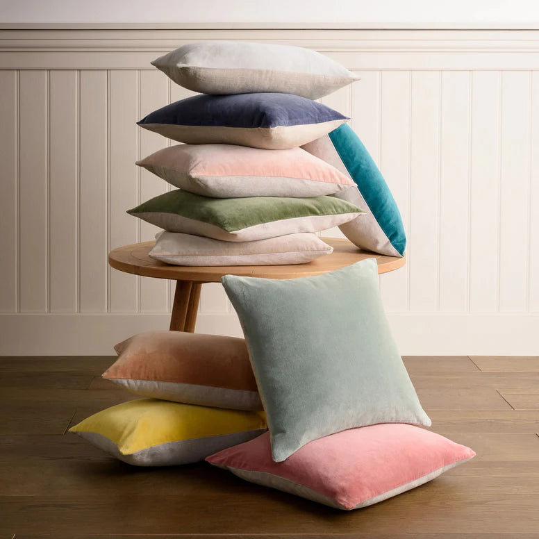 Stack of colorful pillows on a wooden stool against a white paneled wall.