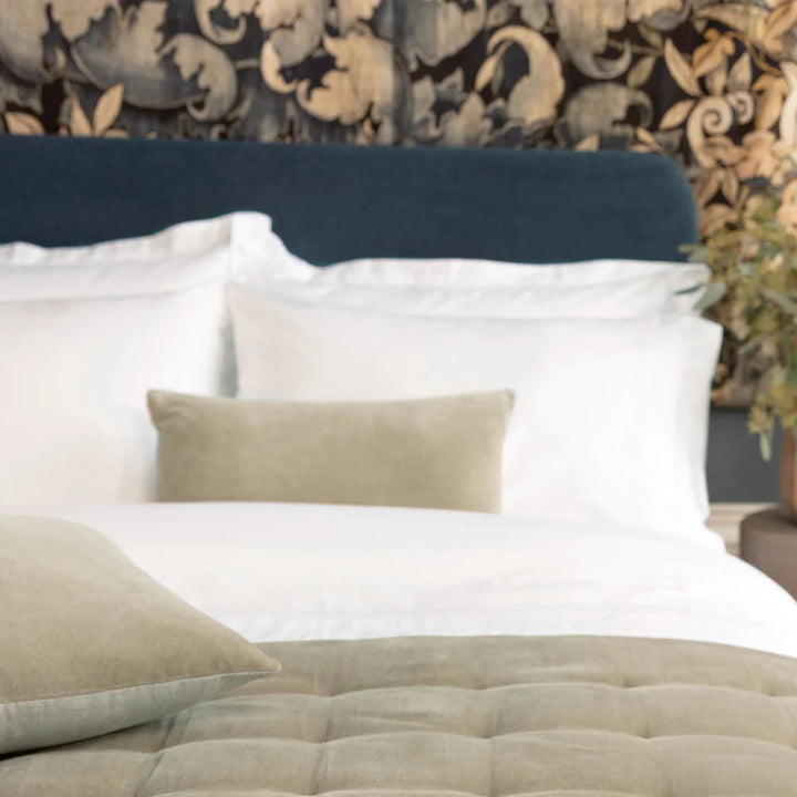 Bed with white pillows and a beige quilt against a decorative wall.