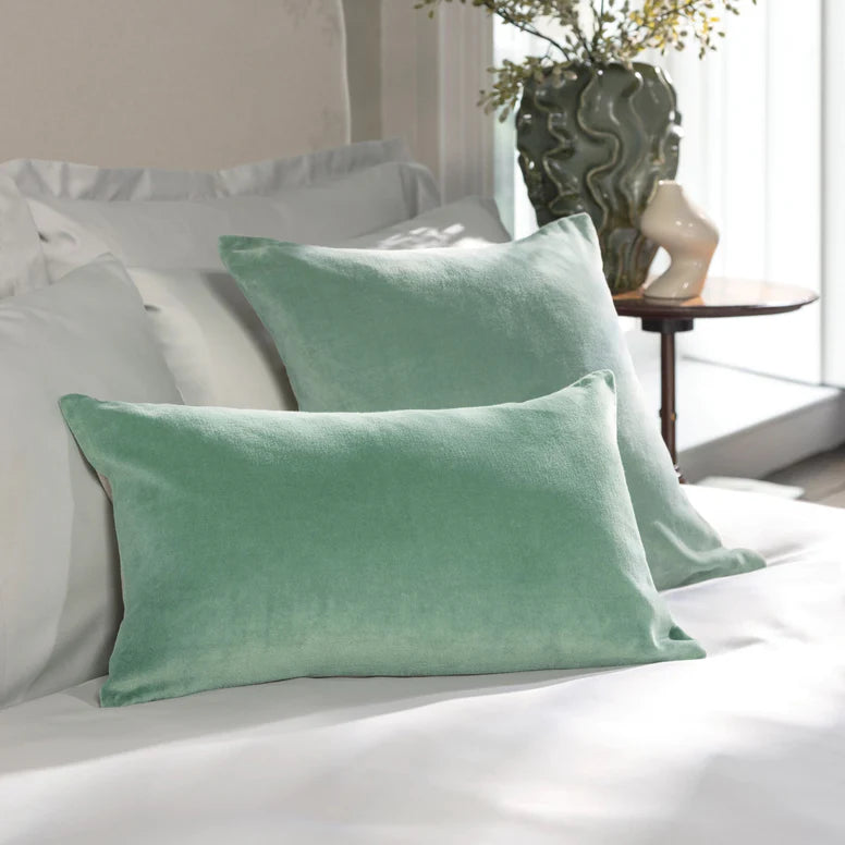 Green pillows on a bed in a bedroom setting with a plant and table in the background.