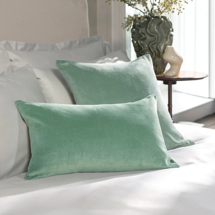 Green pillows on a bed in a bedroom setting with a plant and table in the background.
