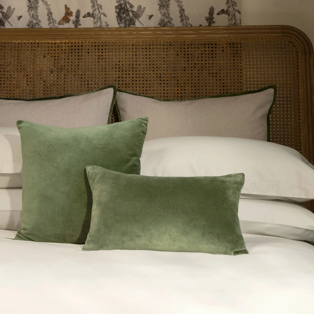 Green velvet pillows on a bed with a wicker headboard