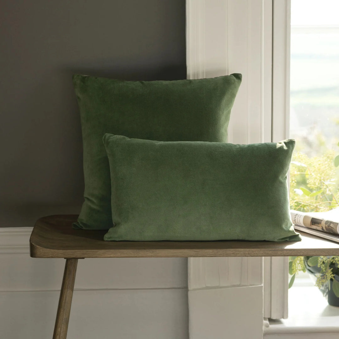 Two green pillows on a wooden stool by a window with natural light.
