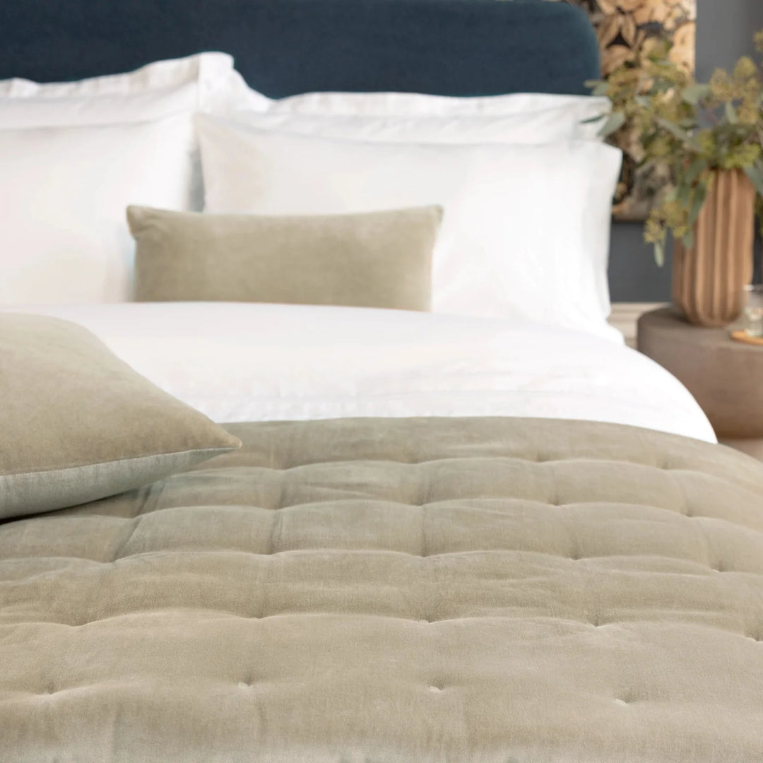 Beige quilted mattress cover on a bed with white pillows and a dark headboard.